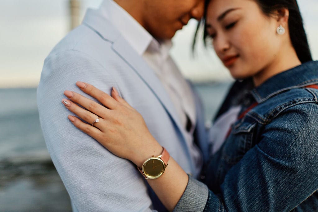 A couple hugs by the Tagus river, as part of a romantic photoshoot after a marriage proposal in Lisbon, Poerugal