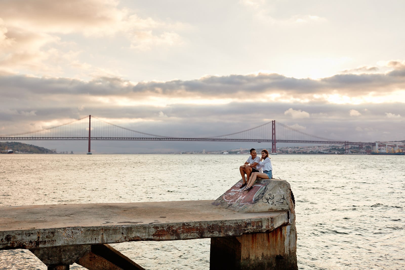 Eliza Sam and Joshua Ngo sit at the old docks on the southern bank of the Tagus river in Lisbon at sunset