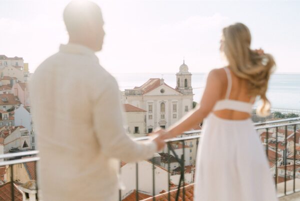 A couple hold hands while enjoying the view at Alfama's viewpoint in early morning light, during a couple photoshoot