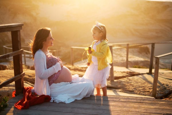 mother and daughter smile at each other in the golden light of the late afternoon during a pregnancy shoot on the beach in Portugal