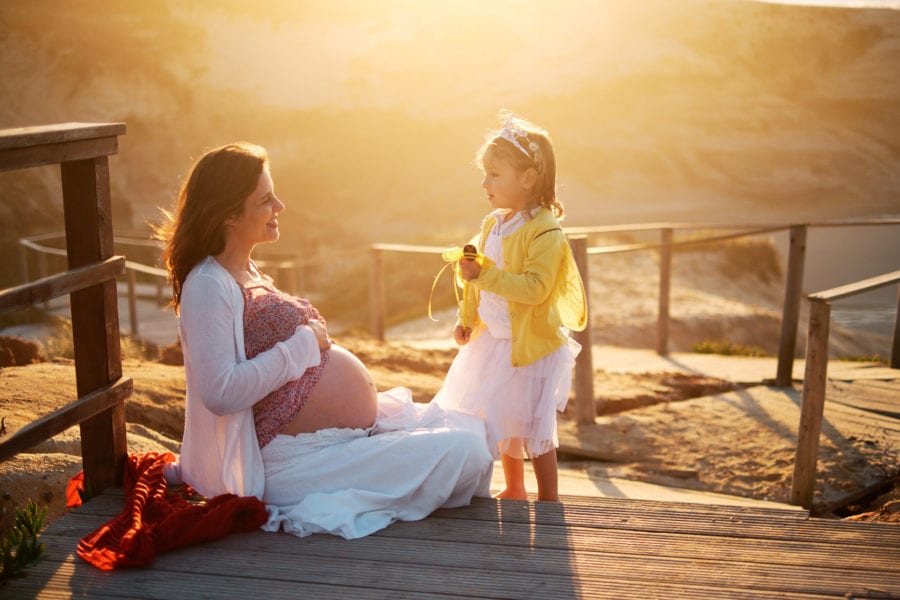 mother and daughter smile at each other in the golden light of the late afternoon during a pregnancy shoot on the beach in Portugal