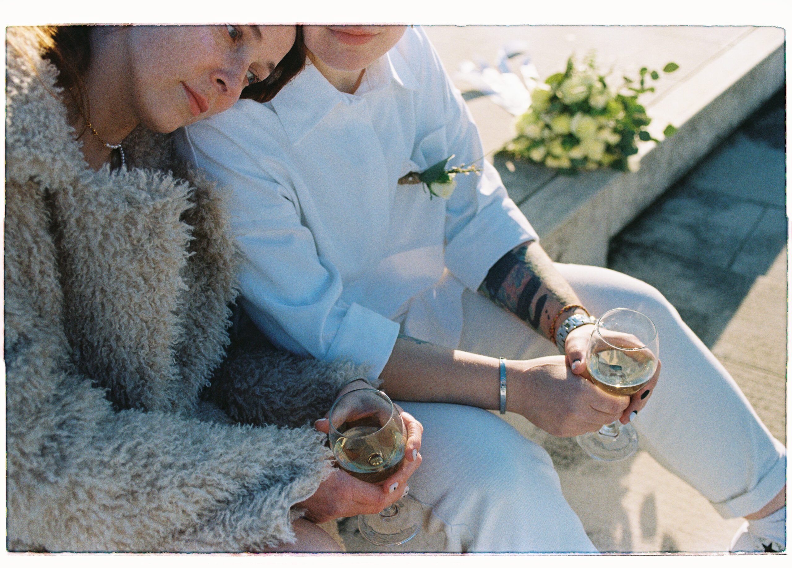 two brides drink a glass of white whine on their elopement day in a photo shot on film